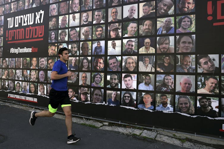 A man in shorts runs past a wall with people's faces on it.